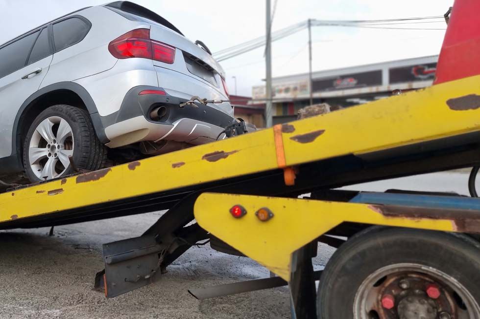 Un SUV argenté sur une rampe de dépanneuse jaune, en cours de chargement après une panne sur le bord de la route.