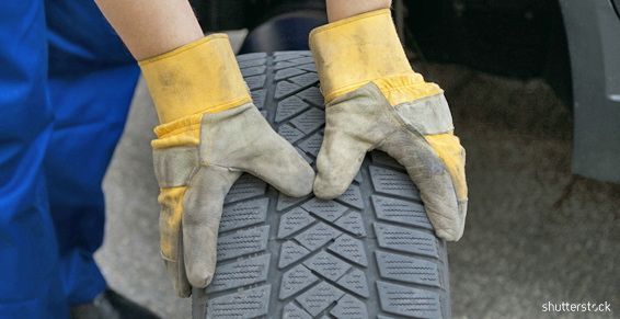 Des mains gantées tiennent la bande de roulement d'un pneu de voiture, en inspectant le dessin du caoutchouc