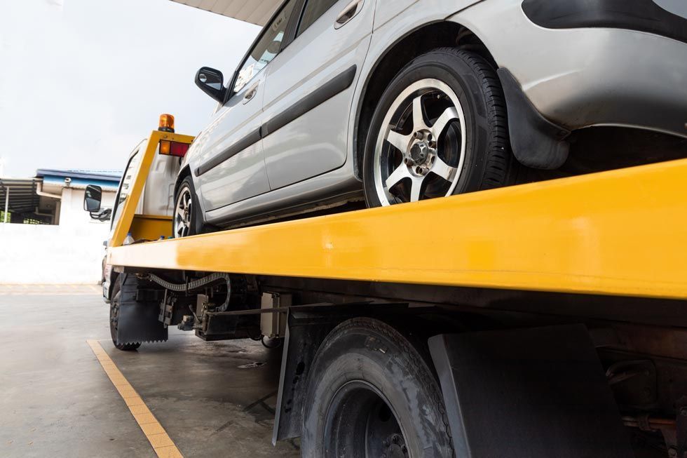 Voiture argentée sur la plateforme d'une dépanneuse jaune en bord de route, vue en contre-plongée