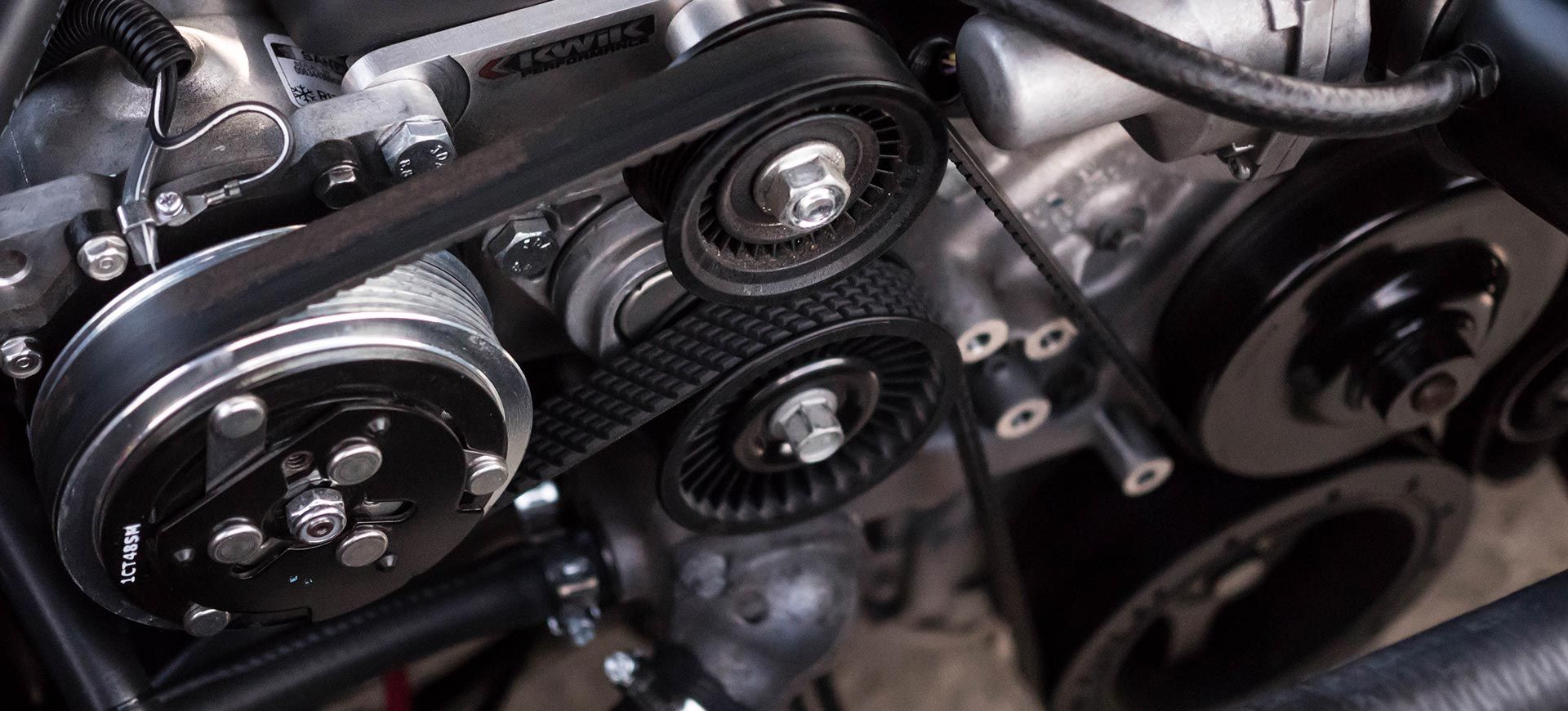 Gros plan sur la courroie serpentine et les poulies d'un moteur de voiture à l'intérieur du compartiment moteur.