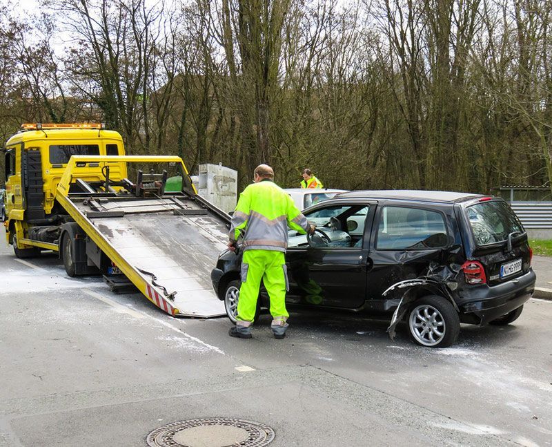 Une dépanneuse charge un SUV noir après un accident de la route ; des ouvriers en tenue de sécurité fluo se trouvent à proximité.