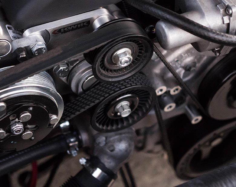 Gros plan sur la courroie serpentine noire et les poulies d'un moteur à l'intérieur d'une voiture.