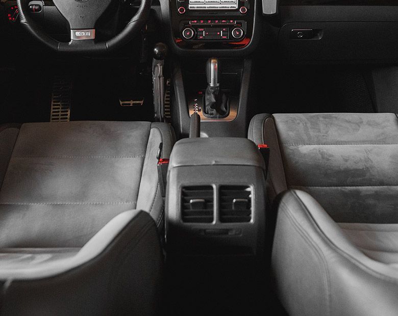 Intérieur de voiture avec sièges noirs et gris, console centrale et tableau de bord, vu depuis la banquette arrière