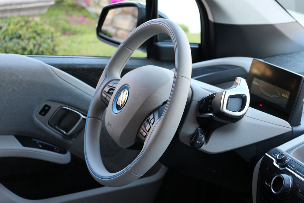 Intérieur de la voiture avec volant, tableau de bord et rétroviseur latéral ; housse de siège bleue visible.