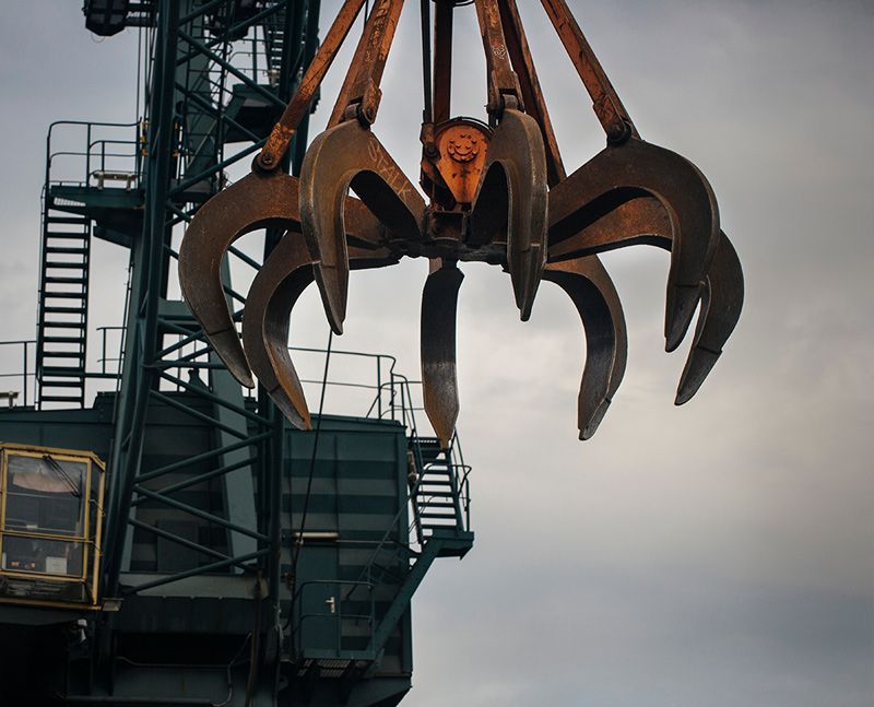 Une grande pince industrielle orange est suspendue à une grue à côté d'une plateforme métallique se détachant sur un ciel gris.