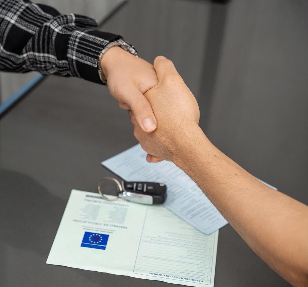 Une poignée de main au-dessus d'une table où se trouvent des documents et une clé de voiture, suggérant un accord commercial.