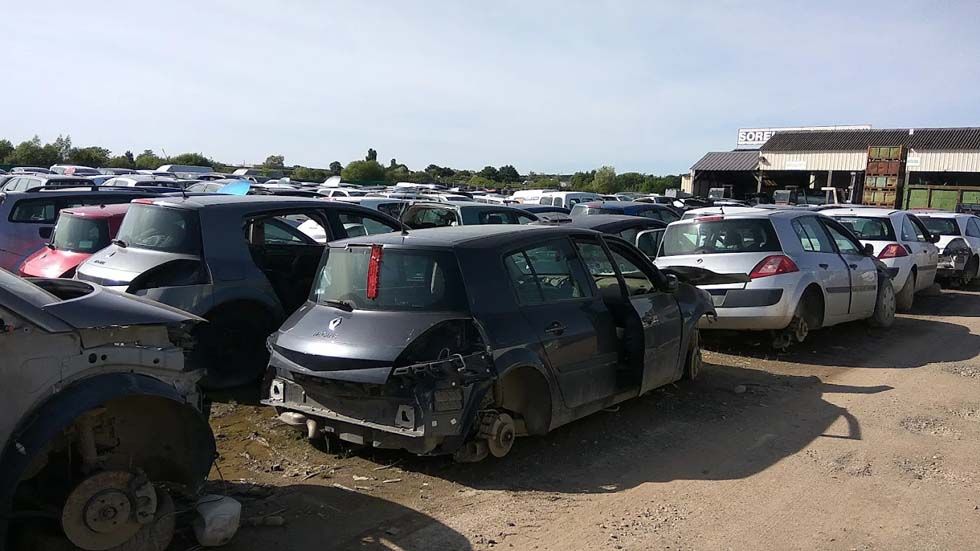Voiture noire à hayon endommagée sur un parking extérieur bondé, avec des rangées de véhicules stationnés.