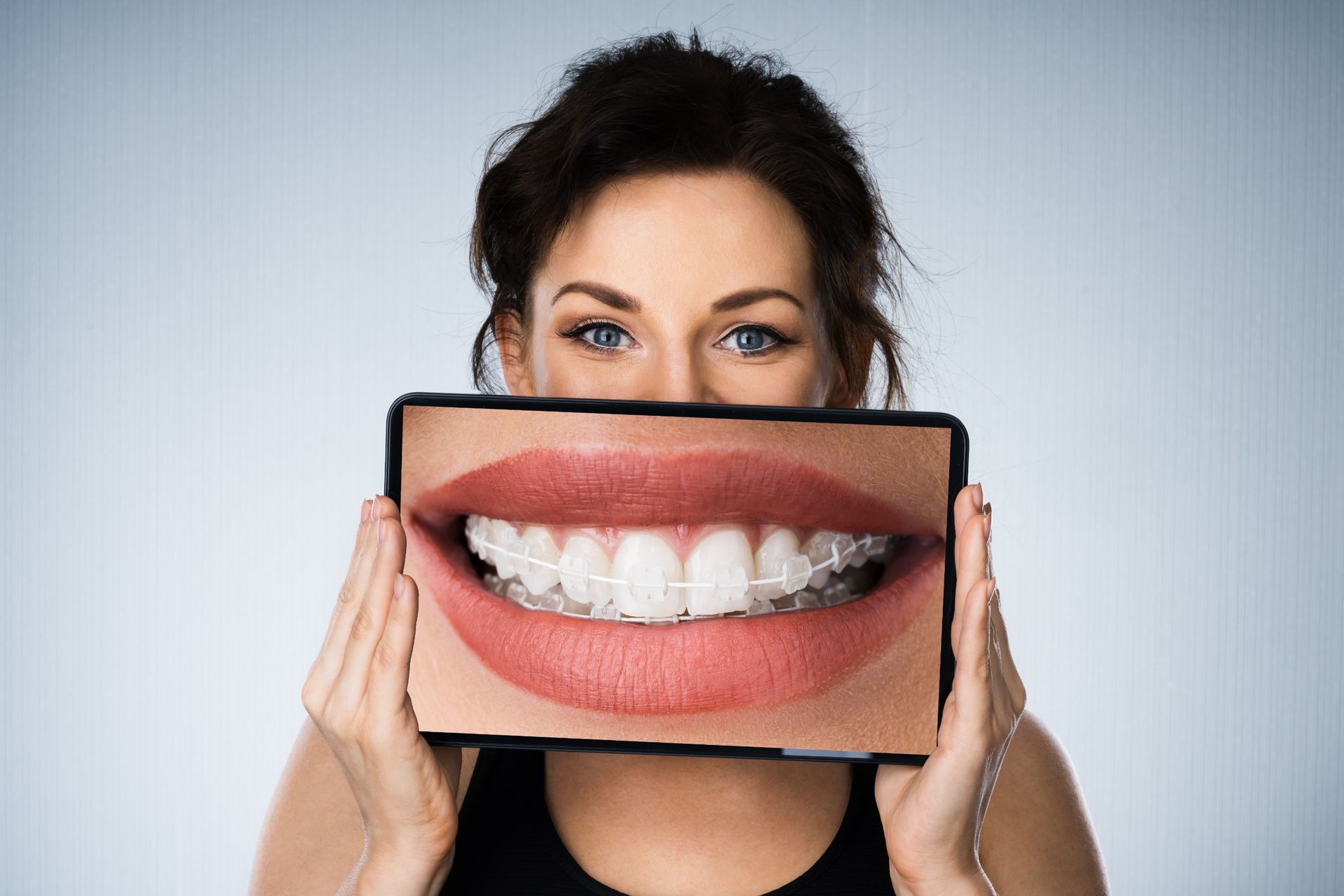 Una mujer sostiene una foto de sus dientes frente a su cara.