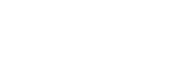 Ein kleiner, hellbrauner Hund mit schwarzer Schnauze und Schlappohren sitzt auf einem grünen Teppich und schaut in die Kamera.