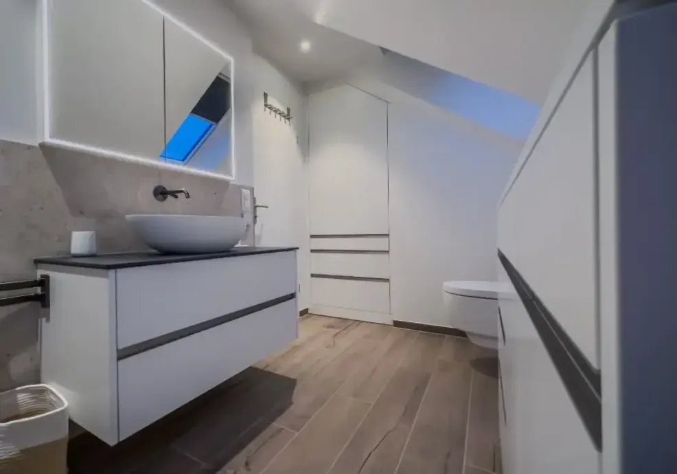 Modernes weisses Badezimmer mit Waschtisch, Waschbecken, Schubladen und Dachschrägen-Dachfenster, Boden in Holzoptik
