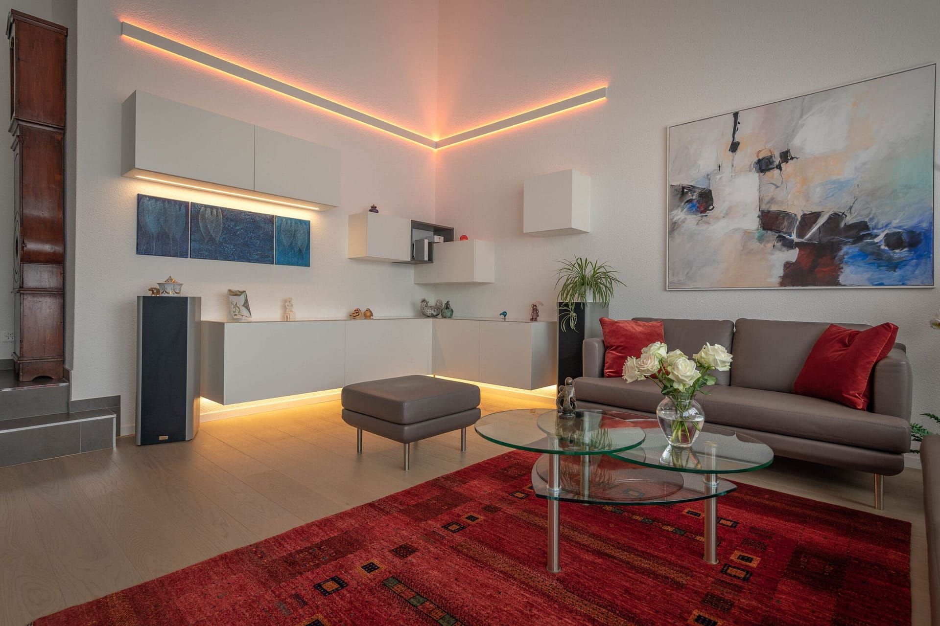 Modernes Wohnzimmer mit rotem Teppich, grauem Sofa, Glastisch und warmer Deckenbeleuchtung