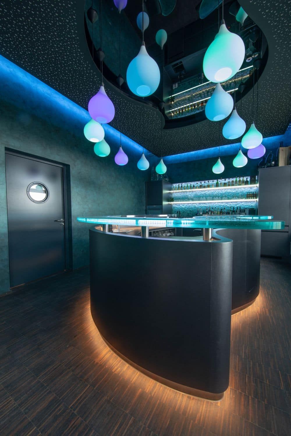 Modernes Bar-Interieur mit geschwungener Theke, blauen Hängelampen und elegantem, dunklem Dekor