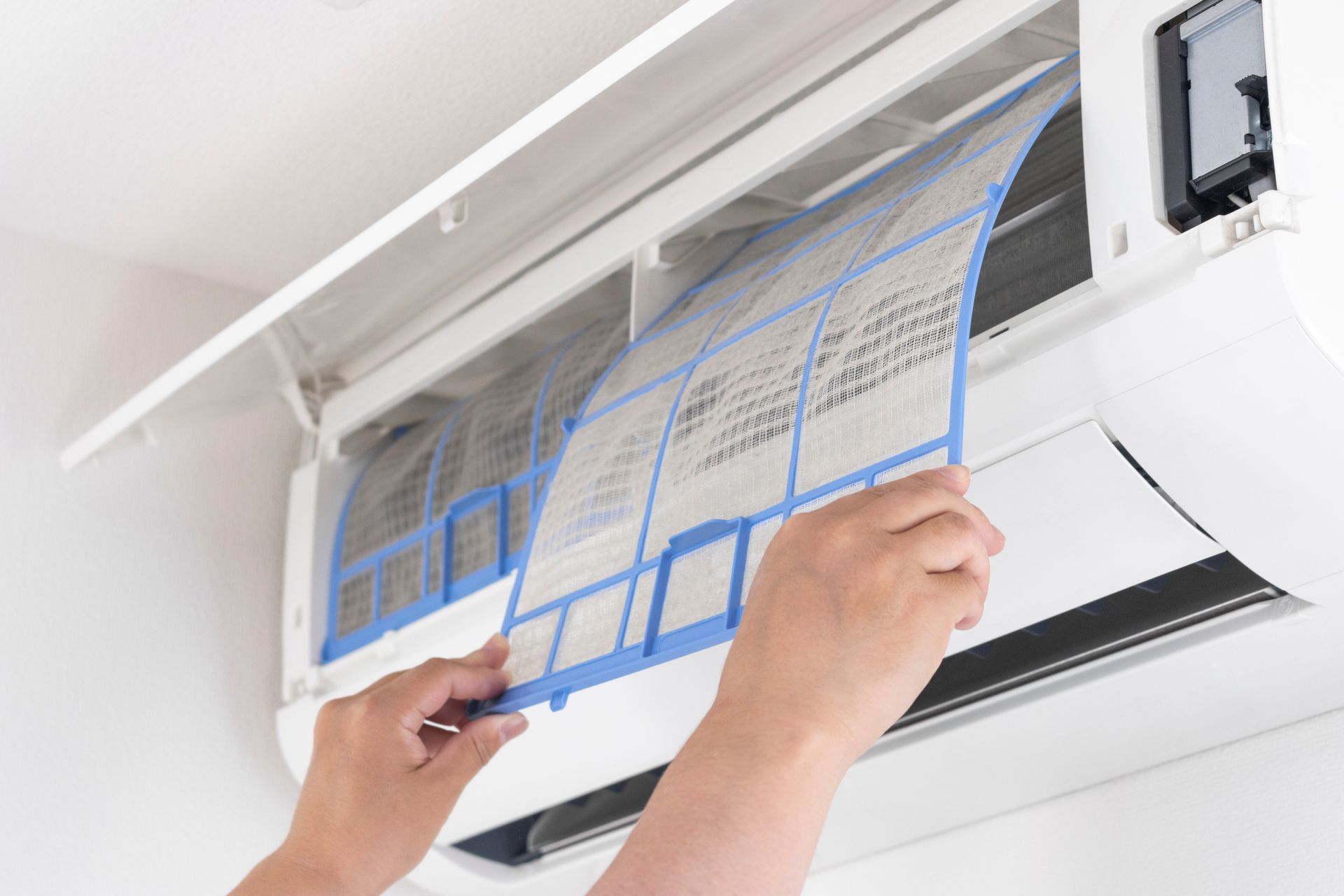 Des mains retirent un filtre de climatiseur à cadre bleu poussiéreux d'un appareil mural pour le nettoyer.