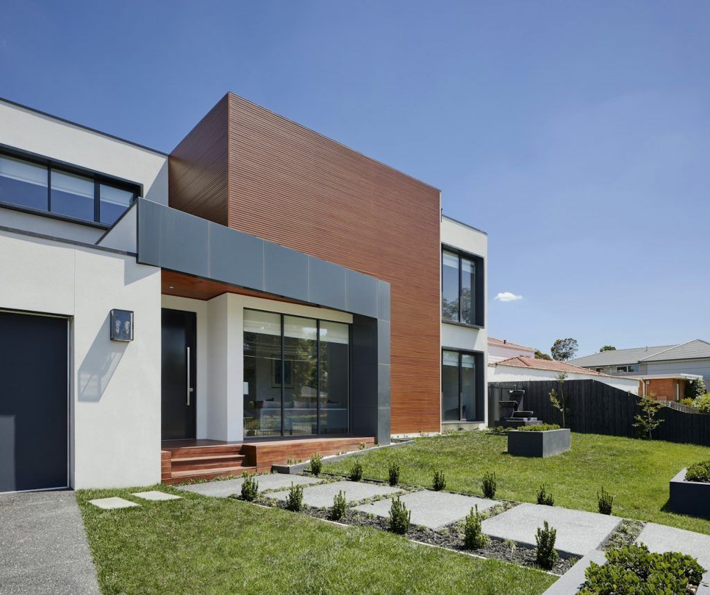 Exterior de casa moderna con paneles marrones, detalles grises y un césped bien cuidado.