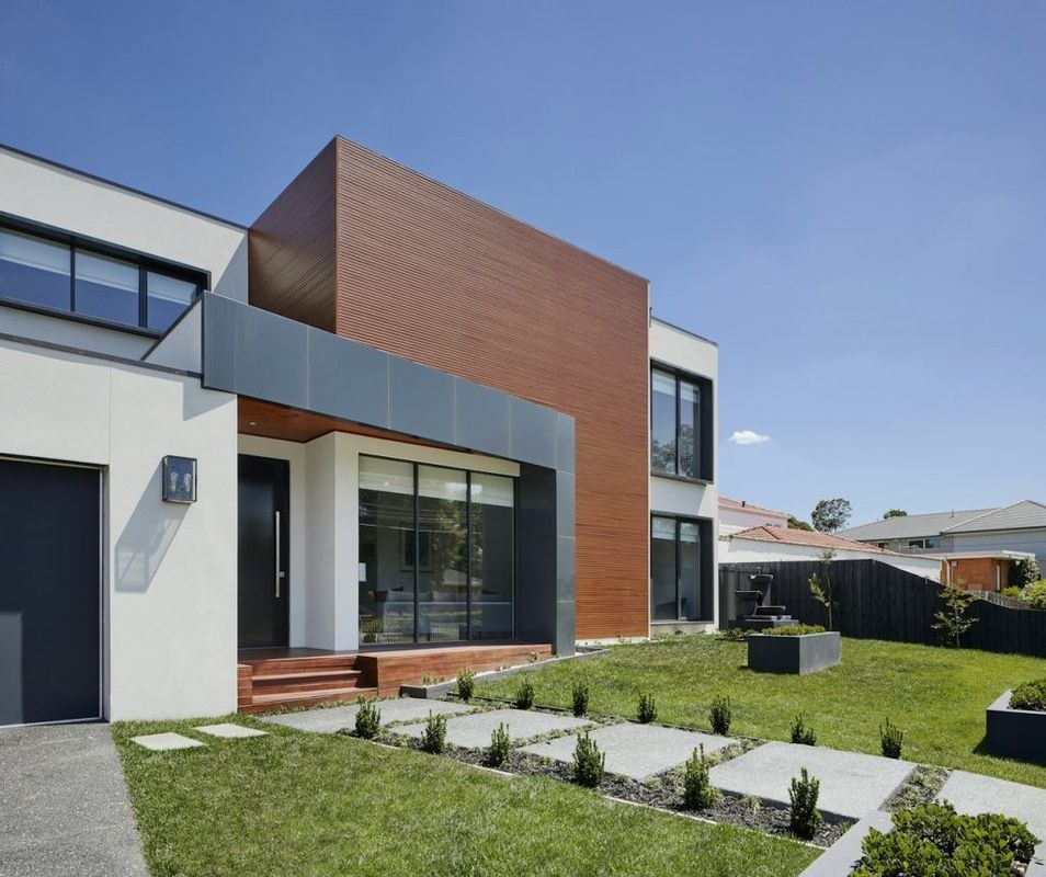 Exterior de casa moderna con paneles marrones, detalles grises y un césped bien cuidado.