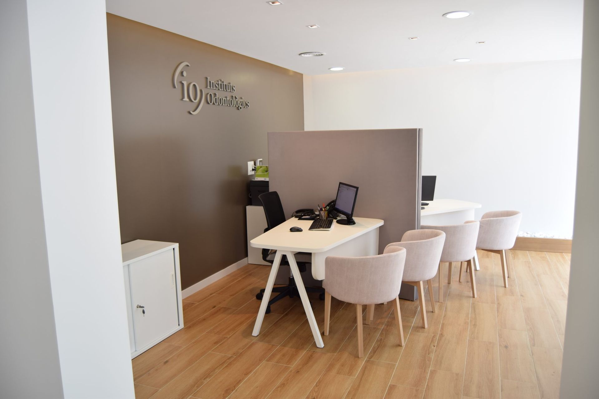 Vista interior de una oficina moderna con escritorios, sillas y el logotipo de una empresa en la pared;