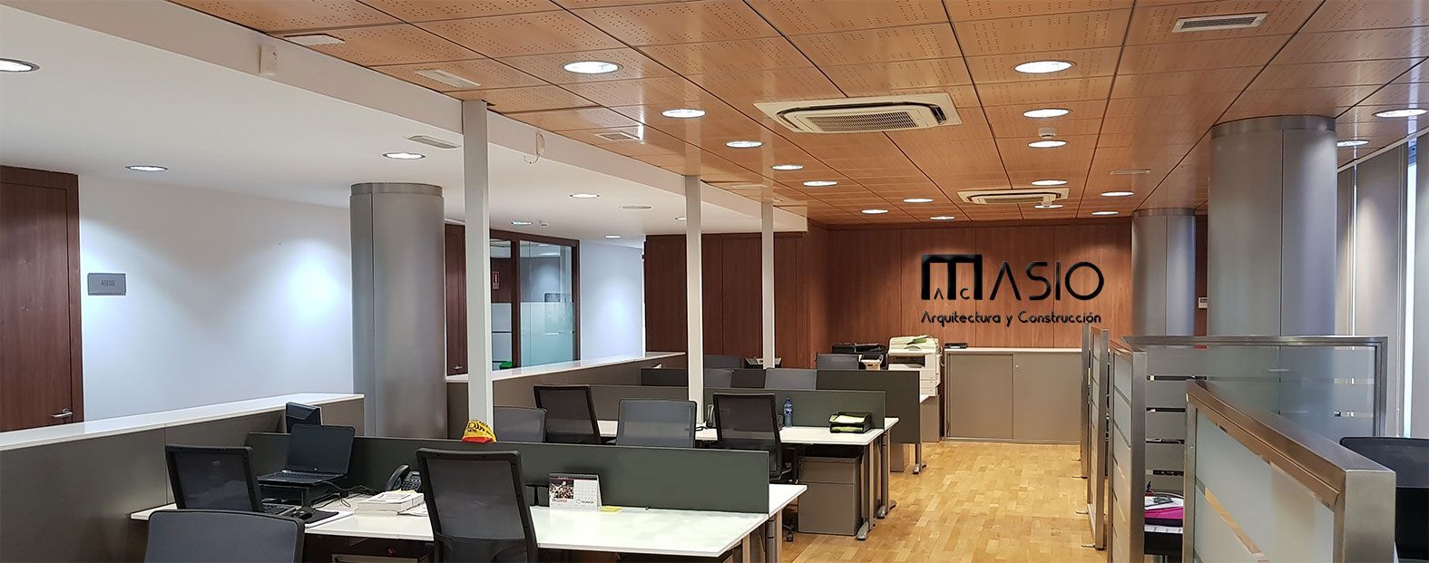 Un espacio de oficina con estaciones de trabajo y el logotipo de MASIO en una pared de madera.