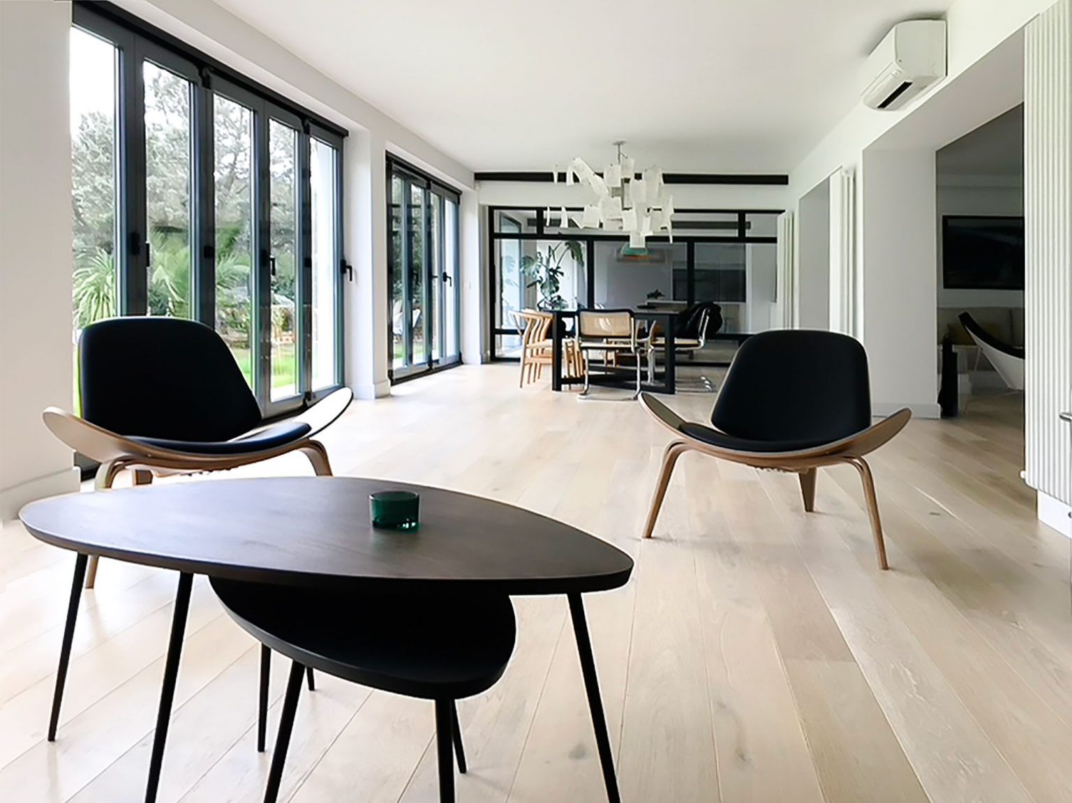 Moderna sala de estar con suelo de madera, sillas negras y una mesa de centro triangular.