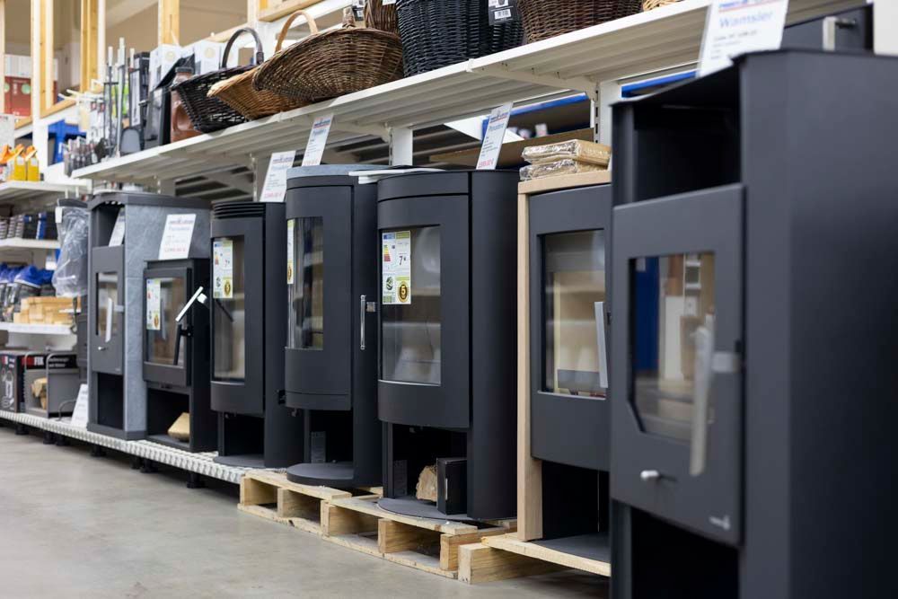 Eine Reihe schwarzer Holzöfen mit Glastüren sind in einem Geschäft ausgestellt.