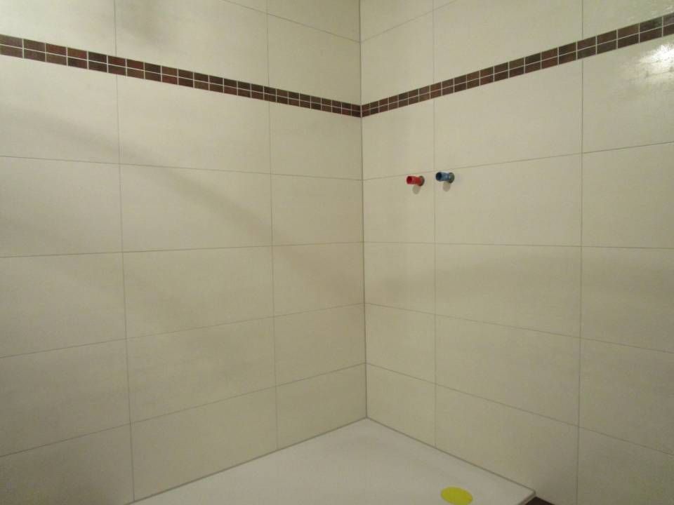 Une salle de bain avec du carrelage blanc et une bande marron sur le mur.