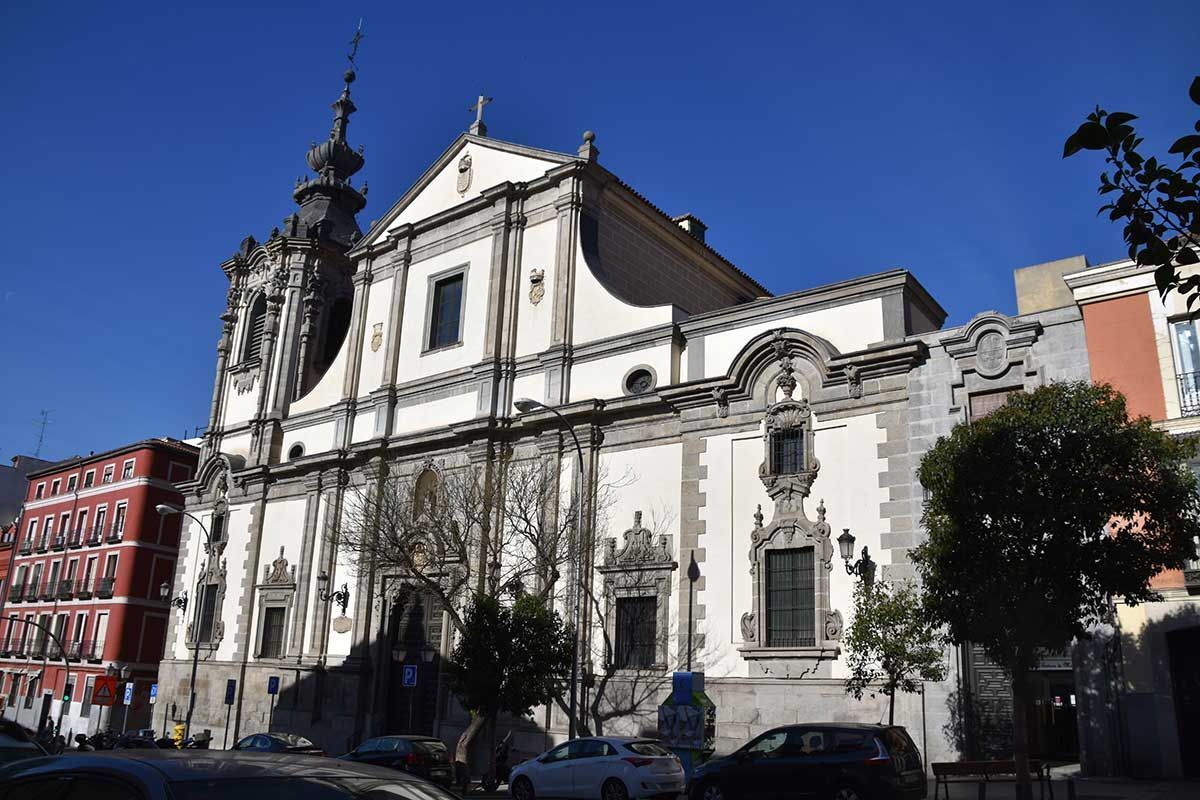 Una toma soleada, desde un ángulo bajo, de una iglesia barroca blanca con una fachada ornamentada, un alto campanario y edificios rojos adyacentes.