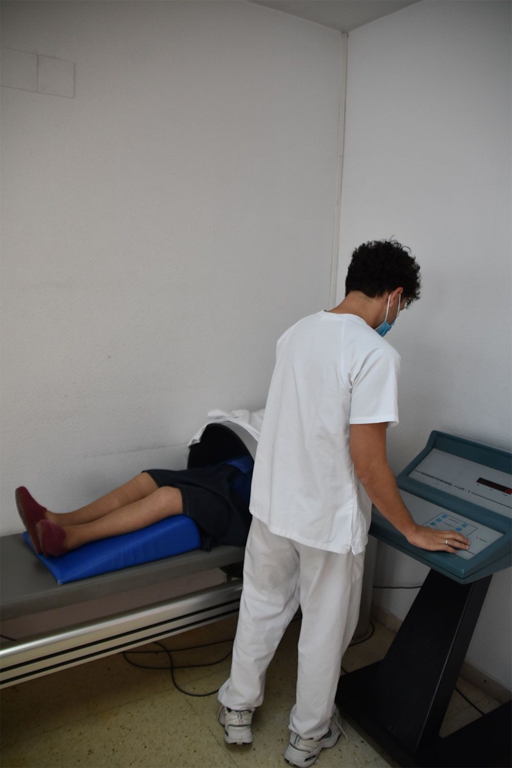 Un médico maneja un panel de control junto a un paciente que yace bajo una máquina de diagnóstico por imagen en un entorno clínico.