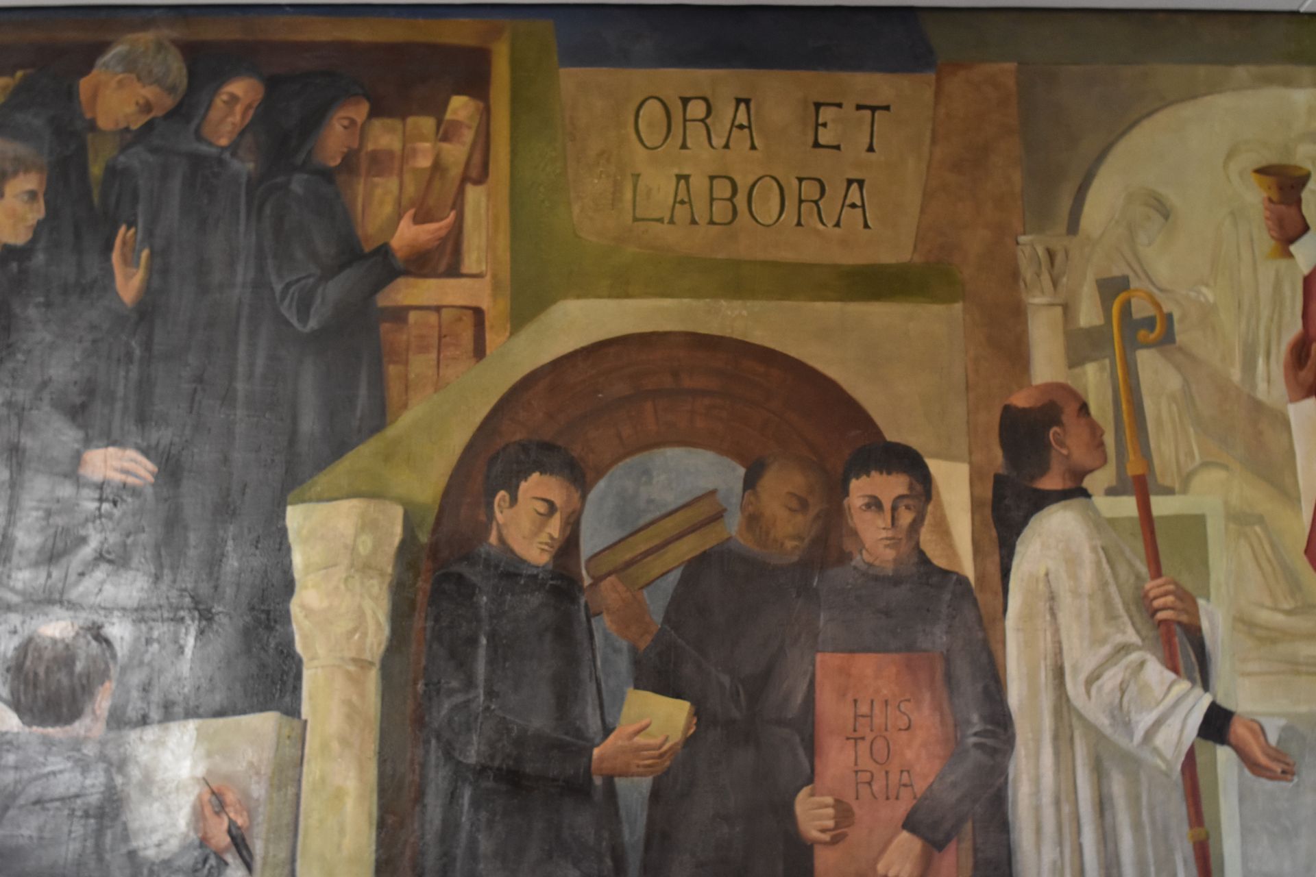 Un mural muestra a monjes estudiando en una biblioteca bajo la inscripción en latín