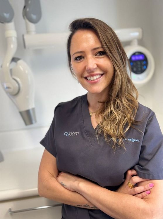 Una mujer en un consultorio dental sonríe con los brazos cruzados.
