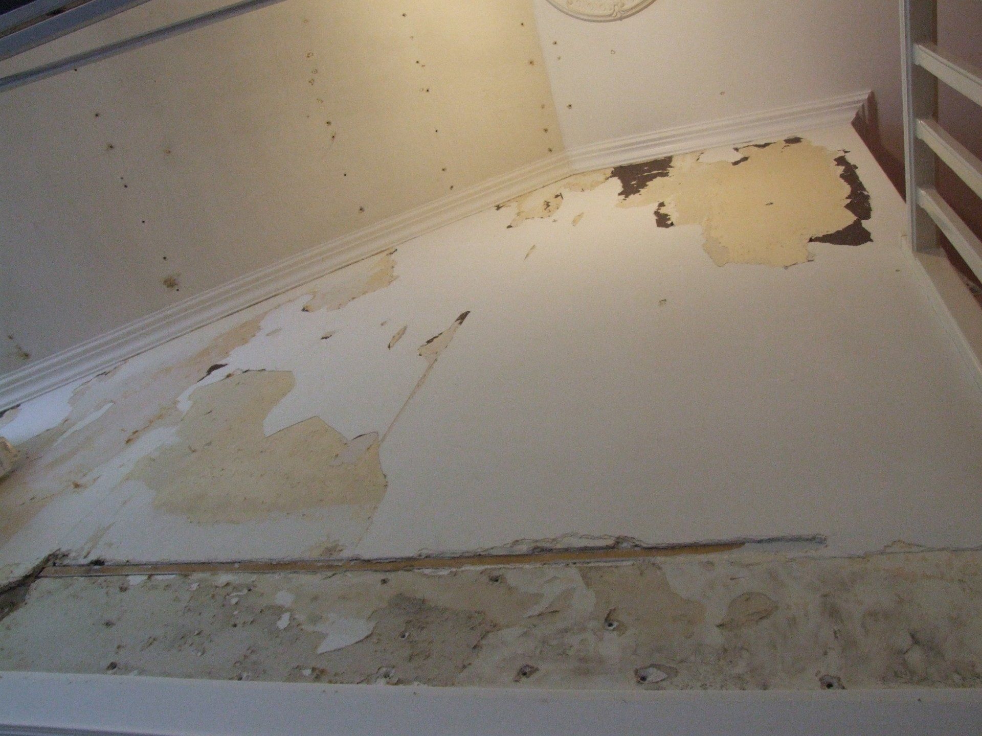 Dégâts d'eau sur un mur et un plafond blancs, avec peinture écaillée et décoloration.