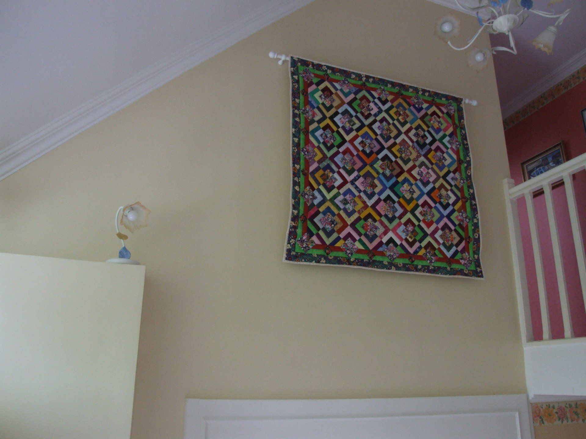 Couette accrochée sur un mur de couleur crème, au-dessus d'une porte et d'un luminaire.