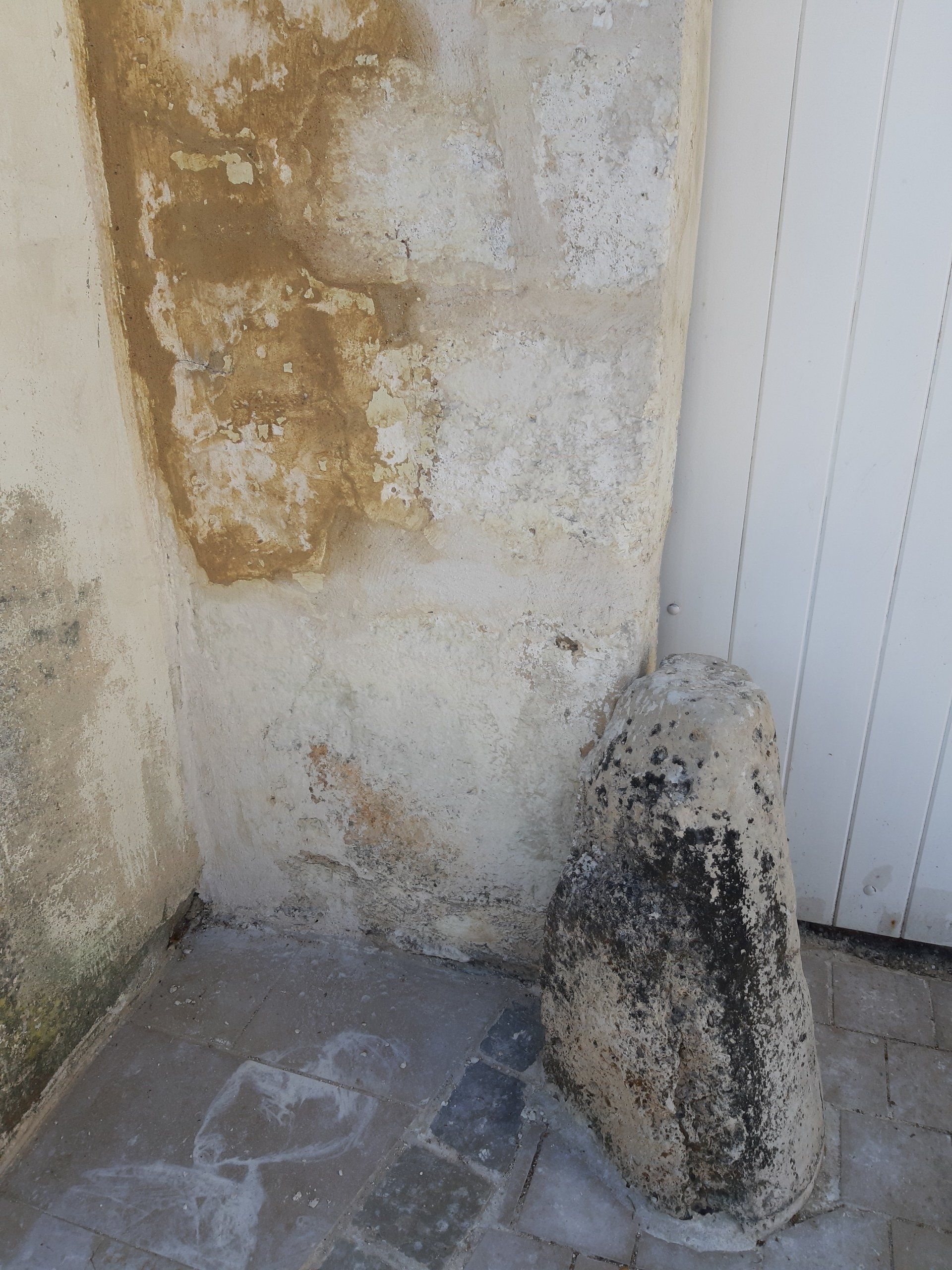 Sculpture en pierre à côté d'un mur en stuc avec des dégâts d'eau et une porte blanche.