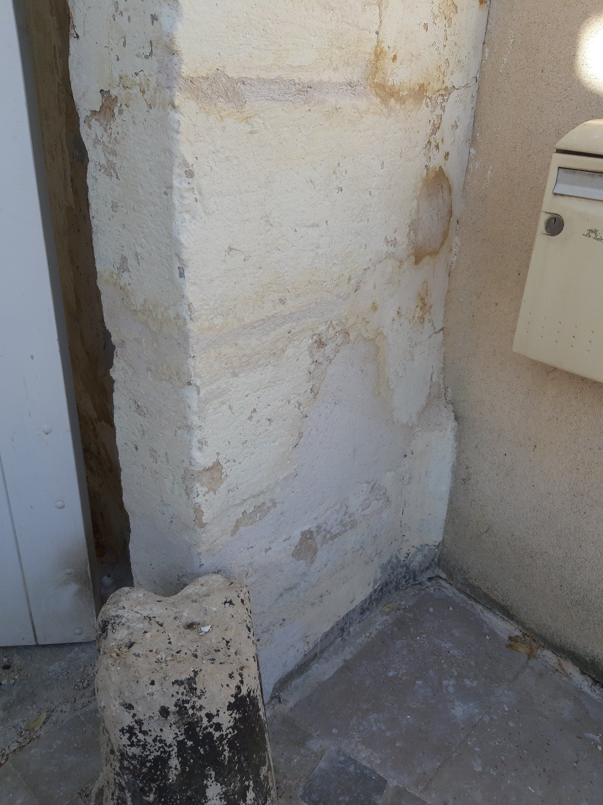 Pilier en stuc blanc à côté d'une porte blanche et d'une boîte aux lettres beige. La base du pilier est gris foncé.