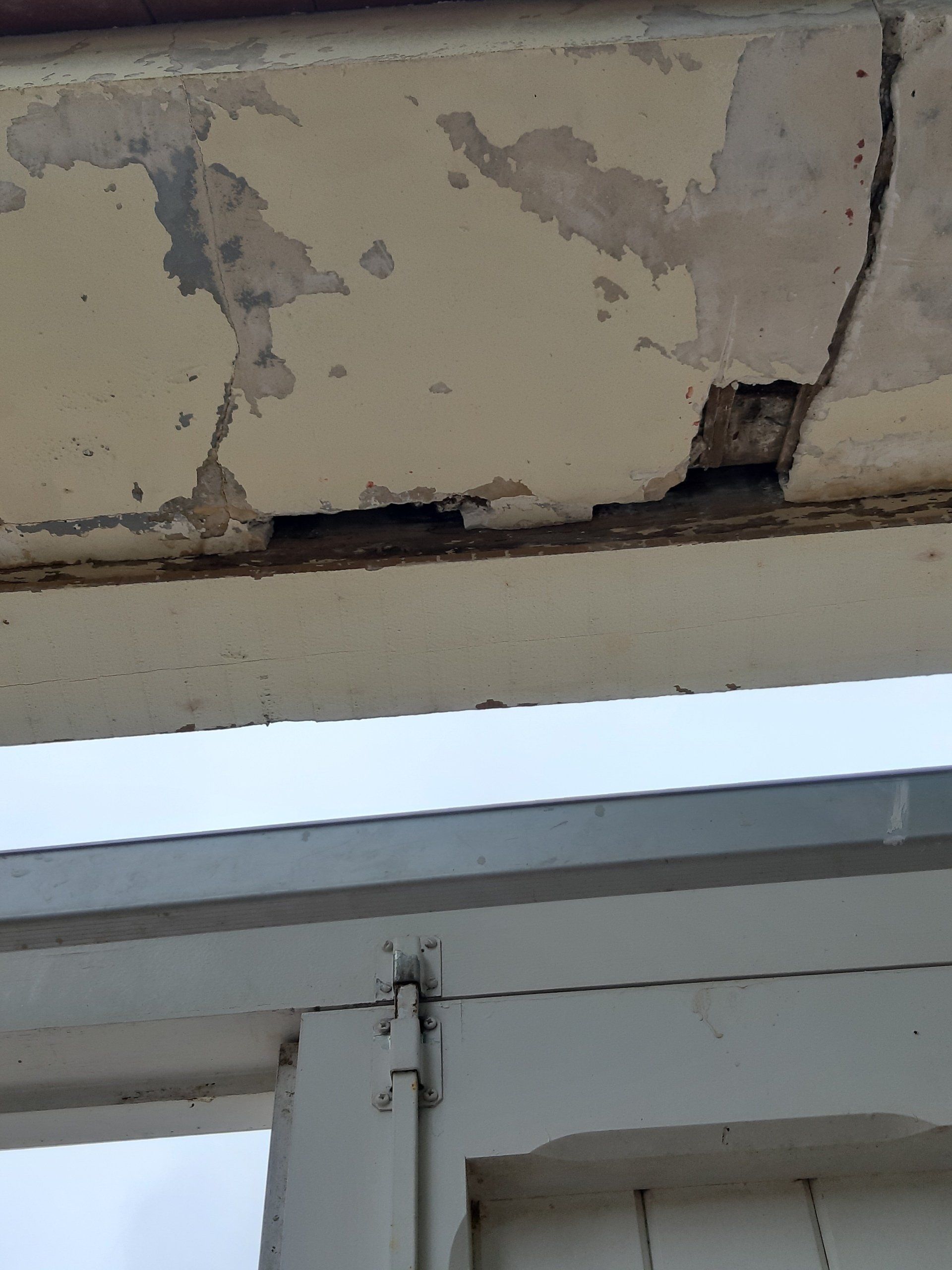 Surplomb en béton endommagé, fissuré et écaillé ; beige clair avec des zones exposées plus foncées.