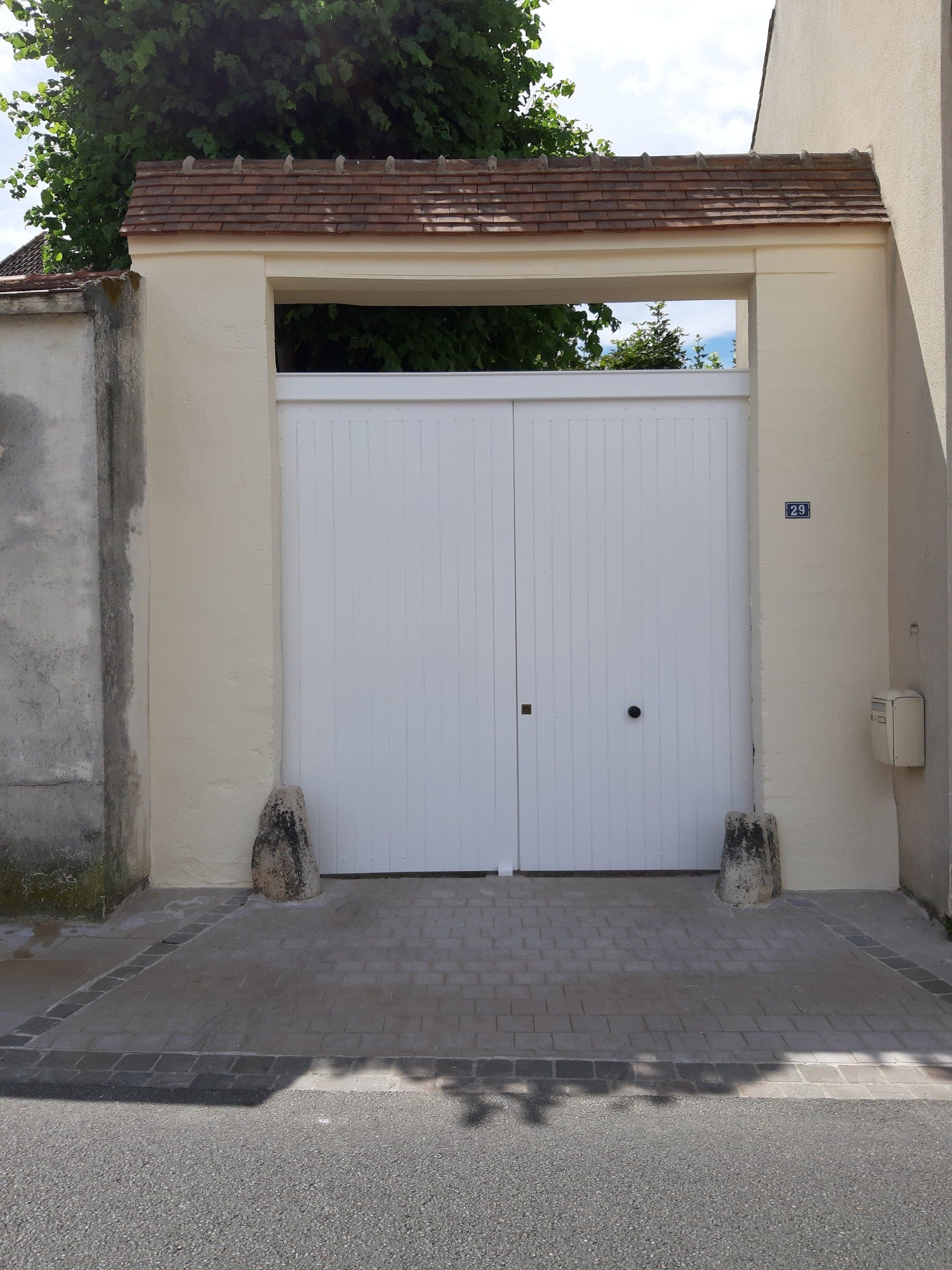 Portail en bois blanc avec une arche beige, encastré dans un mur de couleur claire.