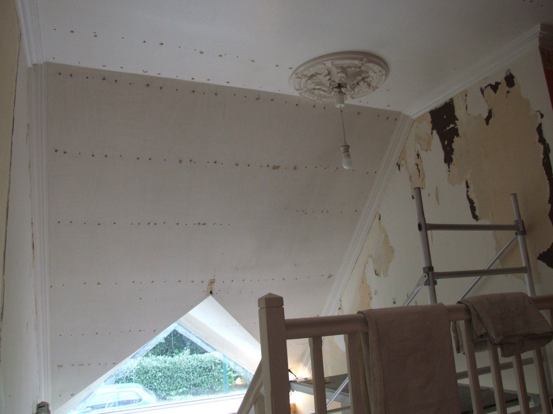 Rénovation intérieure : Plafond incliné, murs avec papier décollé, échafaudage, un escalier et une rosace de plafond.