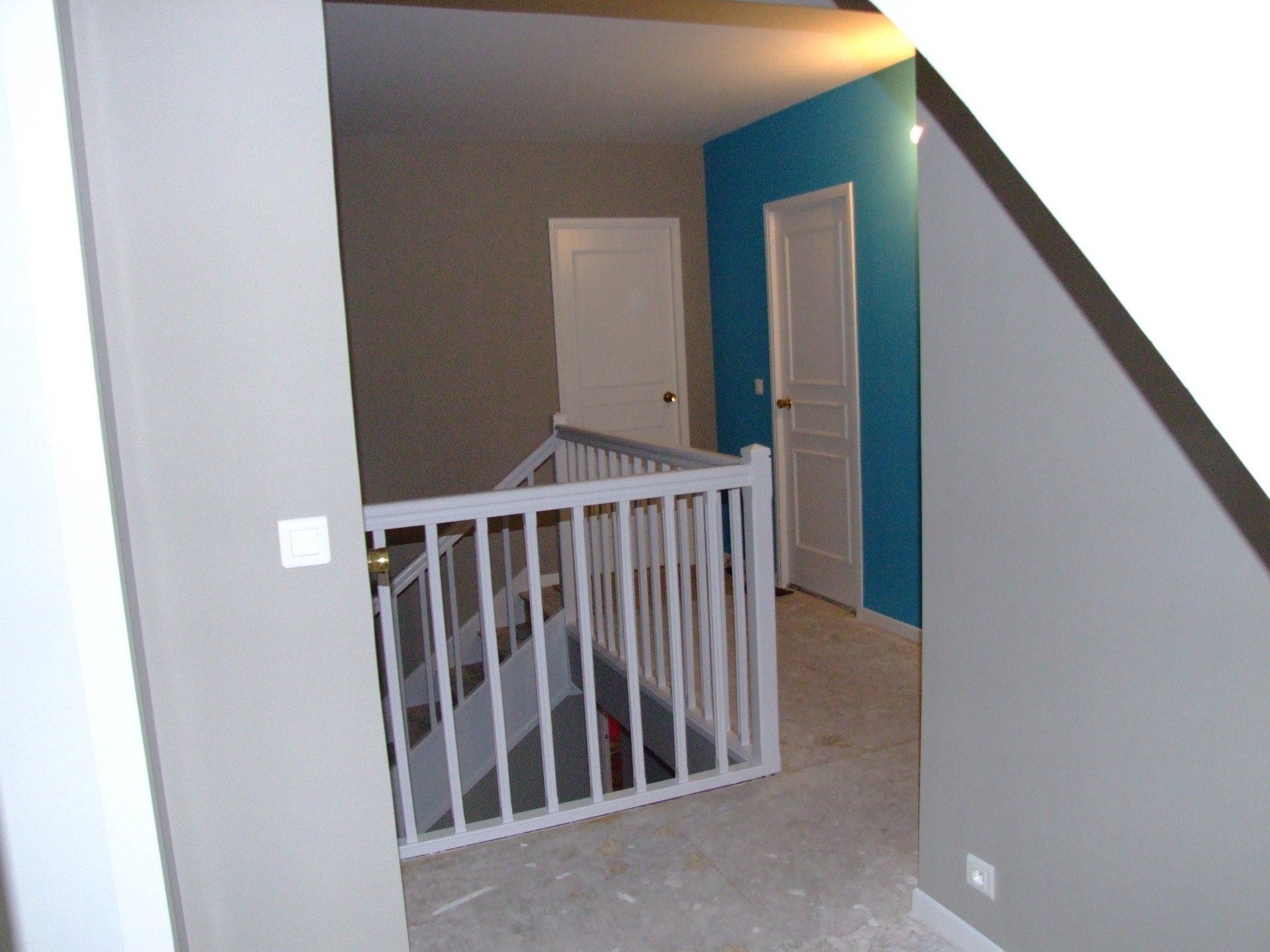 Couloir intérieur avec rampe blanche, murs gris et bleus et deux portes blanches.