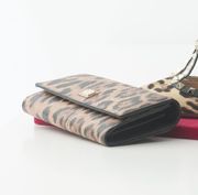Carteira com estampa de leopardo sobre superfície vermelha, com um sapato ao fundo.