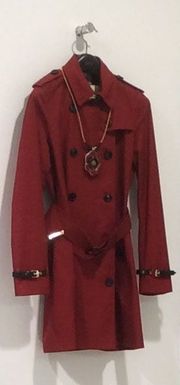 Um sobretudo vermelho com um cinto e um colar pendurados em um gancho de parede.