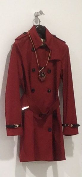 Um sobretudo vermelho com um cinto e um colar pendurados em um gancho de parede.