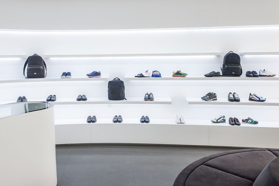 Prateleiras brancas exibindo sapatos e mochilas em um ambiente de loja moderno.