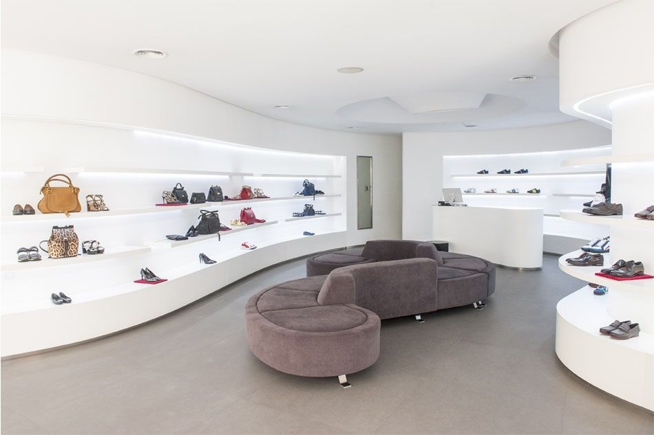 Interior de uma loja de sapatos moderna com prateleiras brancas curvas e uma área de estar cinza.