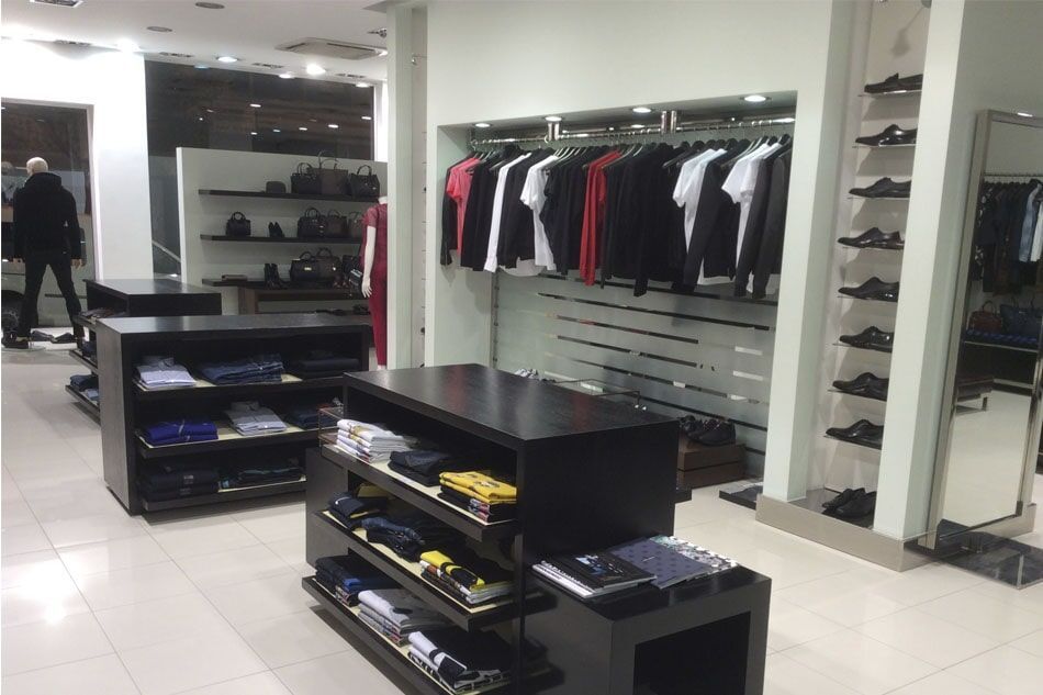 Interior de loja de roupas com araras, prateleiras e uma pessoa olhando as peças.