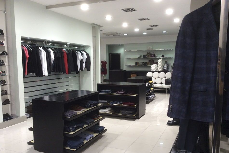 Interior de loja de roupas: prateleiras com camisas e ternos, prateleiras de exposição com itens dobrados.