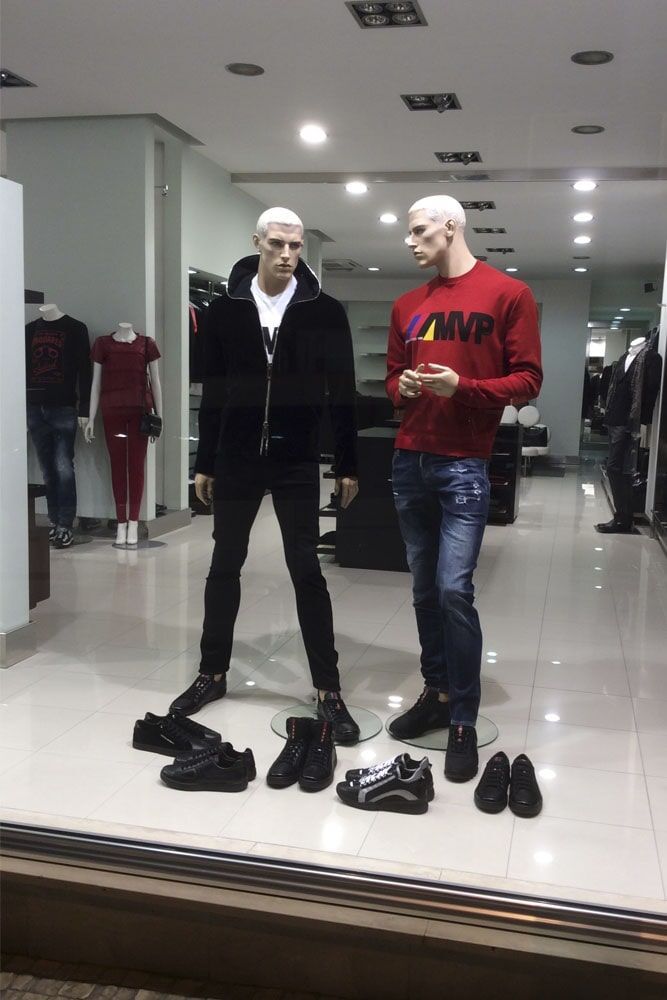 Dois manequins masculinos na vitrine de uma loja vestindo roupas casuais e com vários pares de sapatos na frente deles.