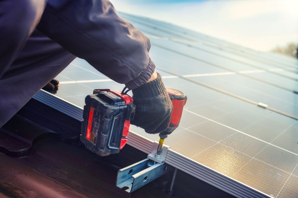 Ein Arbeiter installiert mit einer Bohrmaschine Solarmodule auf einem Dach.