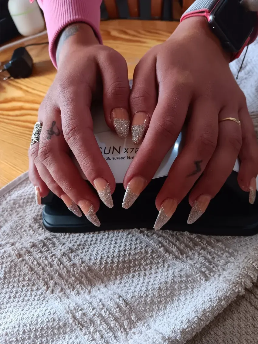 Manos con uñas largas apoyadas sobre un teléfono en una mesa, vestidas con mangas rosas y oscuras.