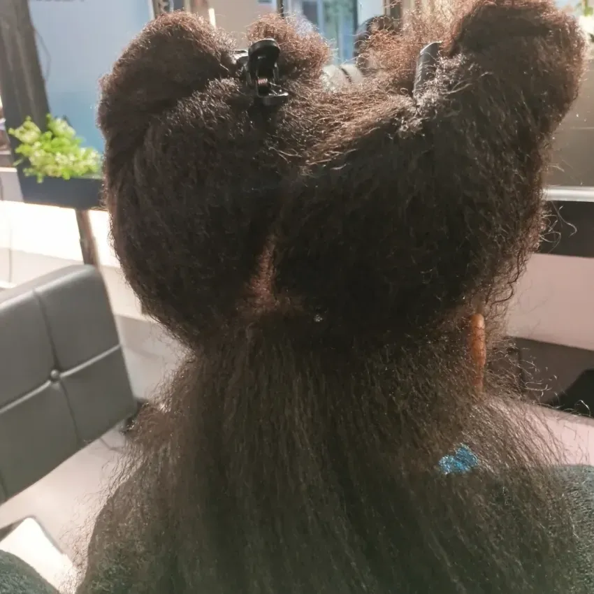 Vista trasera de un niño con dos bollos esponjosos, sentado en el interior de una casa cerca de una ventana.