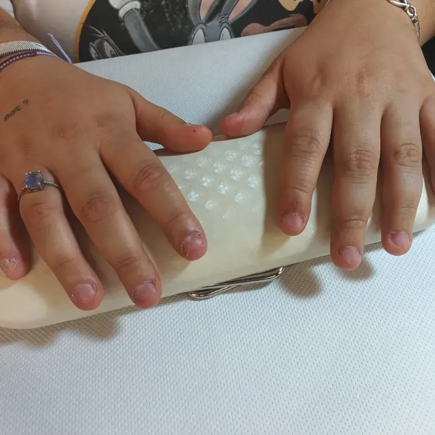 Manos apoyadas sobre un bolso de mano blanco texturizado sobre una mesa.