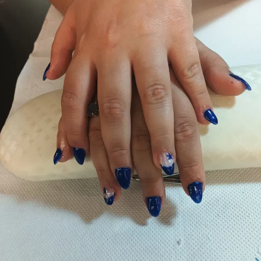Manos con esmalte de uñas azul brillante descansando sobre una superficie blanca texturizada.