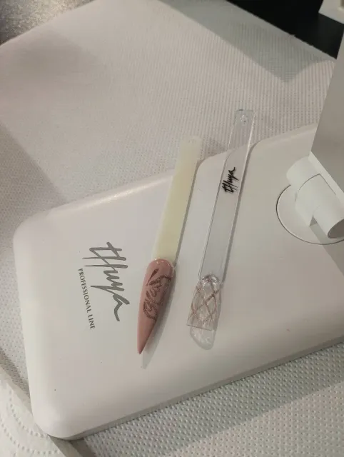 Funda blanca para teléfono con un cortaúñas transparente y una pequeña pieza decorativa rosa sobre una superficie de tela clara.